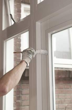 Eine Person streicht ein weißes Fensterrahmen aus Holz mit einem Pinsel und Lack.