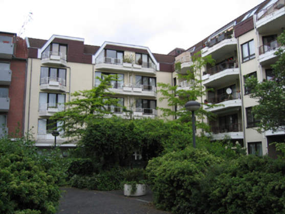 Modernes Mehrfamilienhaus mit Balkonen und begrüntem Innenhof in urbaner Wohnanlage.